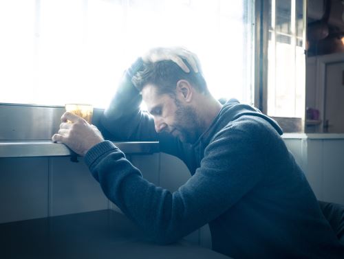 Depressed man leaning against a drink rail with his hand around around a glass