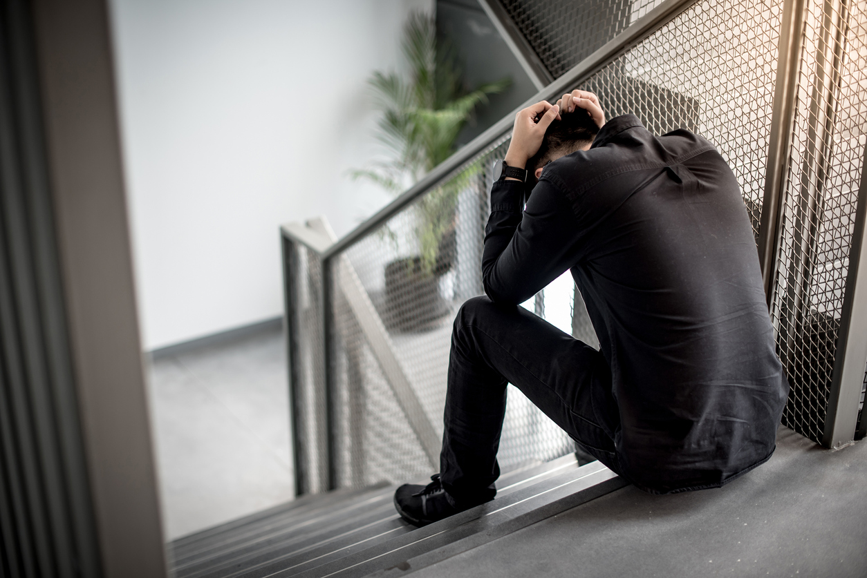 Asian businessman feeling stressed and headache sitting on stair in office building. Depression from business problem. Mental health illness or office syndrome concept