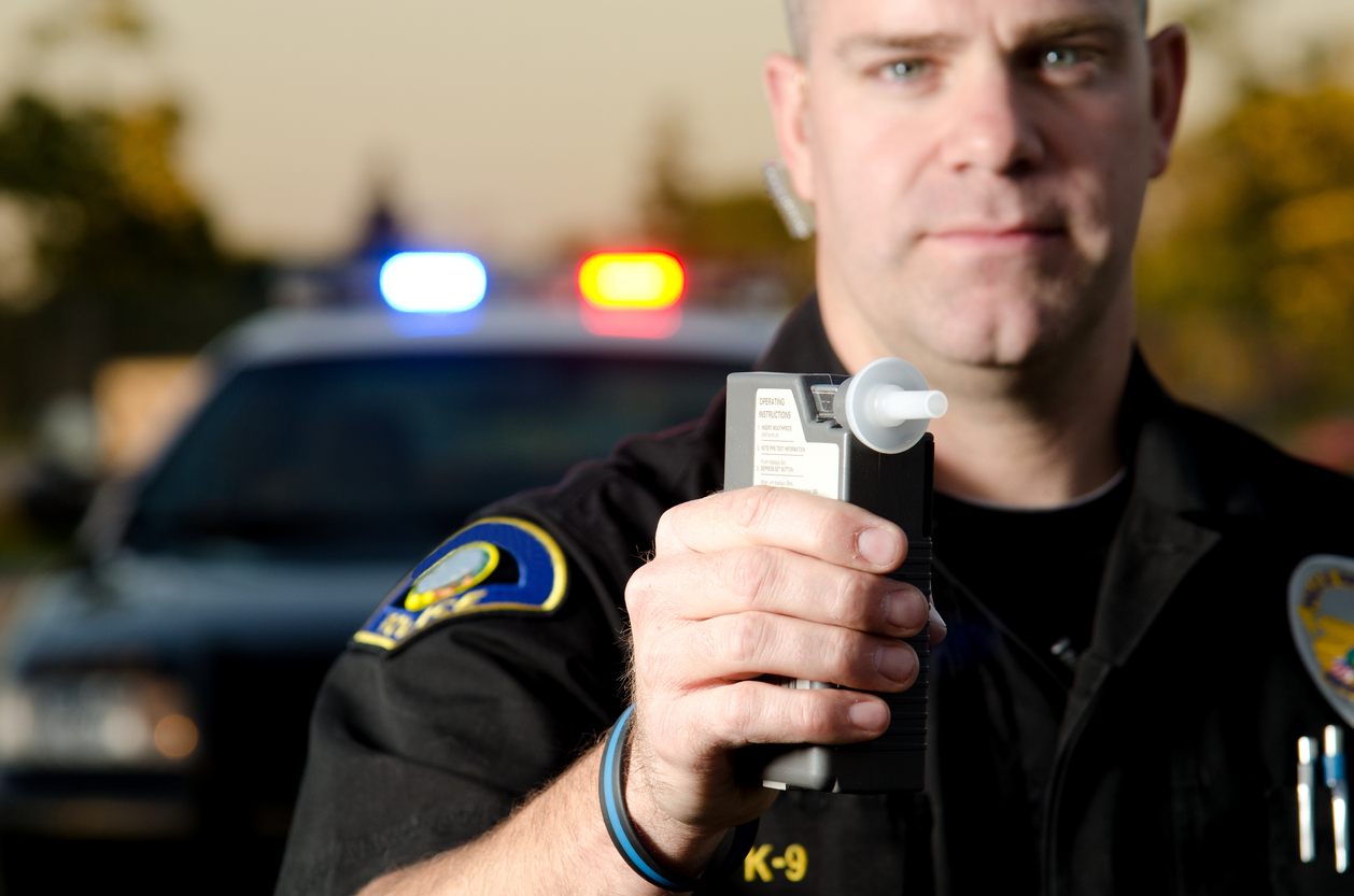 A police officer holds a breath test machine in his hand ready at a traffic stop with his patrol car in the background.*the officer was blurred on purpose to place focus on the mouth piece.