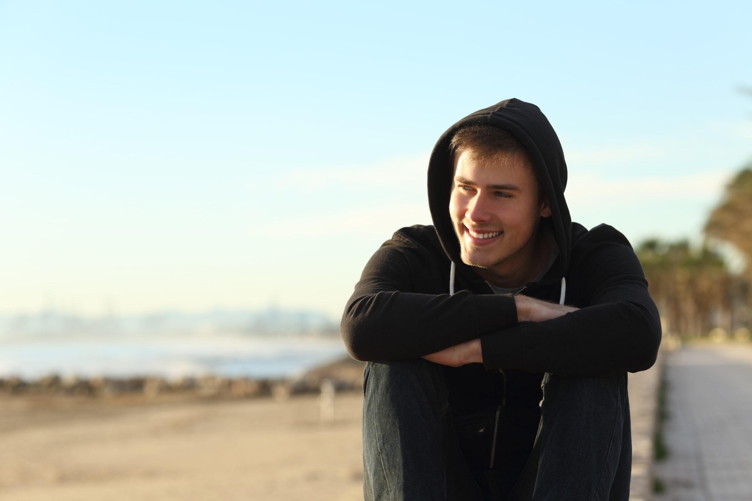 Front view portrait of a teenage boy sitting on the beach looking away