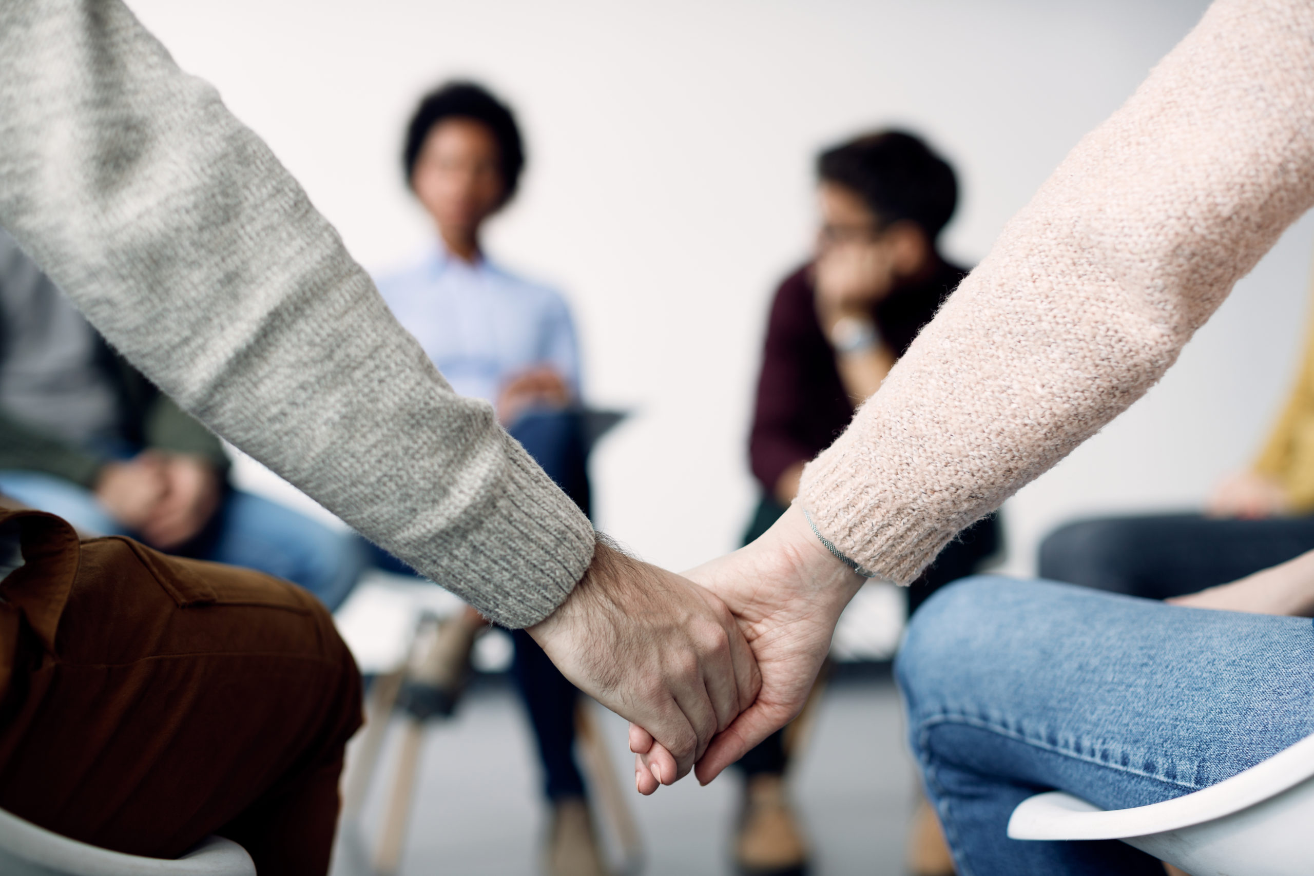 Close-up of couple holding hands while attending psychotherapy with group of people.