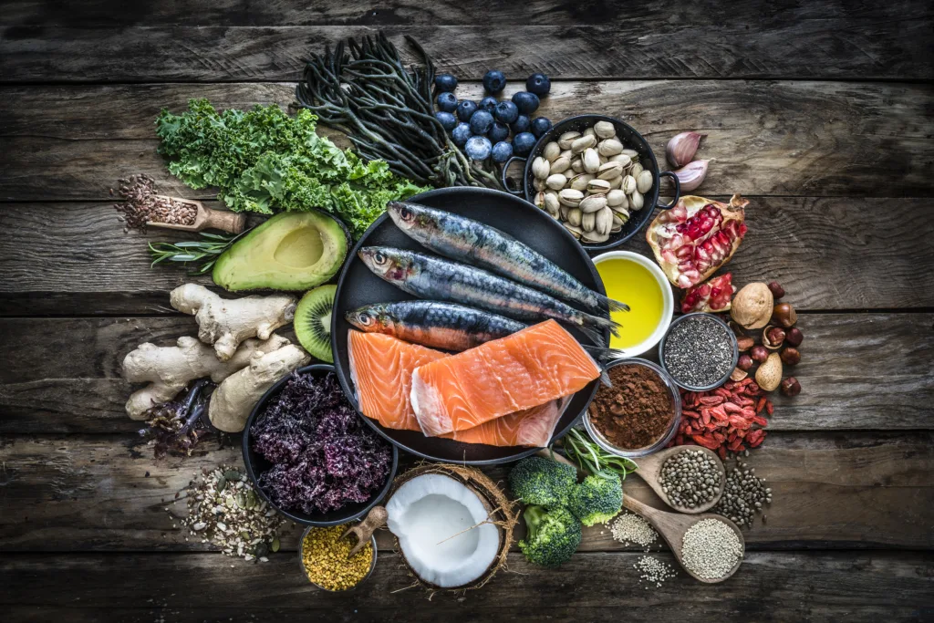 Top view of healthy, antioxidant group of food placed at the center of a rustic wooden table. The composition includes food rich in antioxidants considered as a super-food like avocado, kale, blueberries, chia seeds, coconut, broccoli, different nuts, salmon, sardines, pollen, quinoa, hemp seeds, seaweed, cocoa, olive oil, goji berries, flax seeds, kiwi fruit, pomegranate and ginger. XXXL 42Mp studio photo taken with SONY A7rII and Zeiss Batis 40mm F2.0 CF